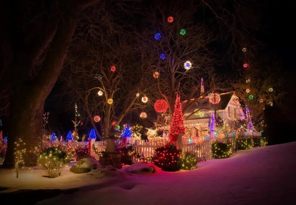 House decorated with colorful Christmas lights, surrounded by snow and festive displays.
