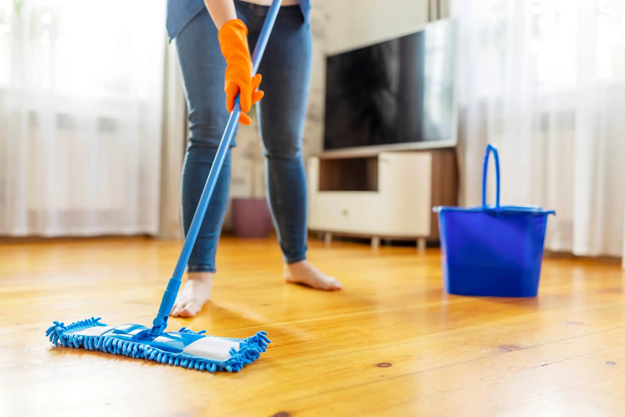 A woman cleans her hardwood floors with a mop and bucket.