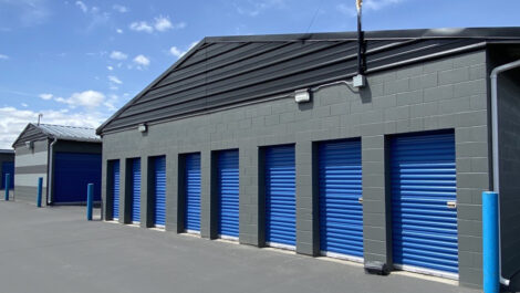 Exterior view of the Glacier West Self Storage facility in Twin Falls, Idaho, showing tan-colored buildings with green trim and multiple storage unit doors.