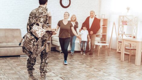Military family reunion as a soldier in uniform approaches a smiling woman, child, and older couple.